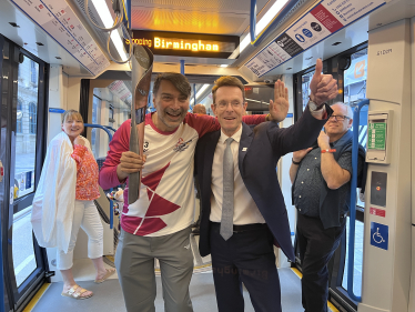 Andy Street with the torch bearer on a tram at the 2022 Birmingham Commonwealth Games